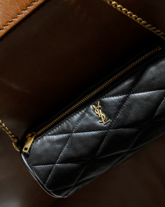 A close-up of a black quilted designer handbag with gold chain and logo.