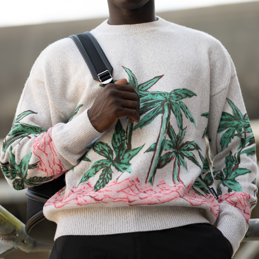 Model wearing a cream sweater with tropical palm print and crossbody bag strap.