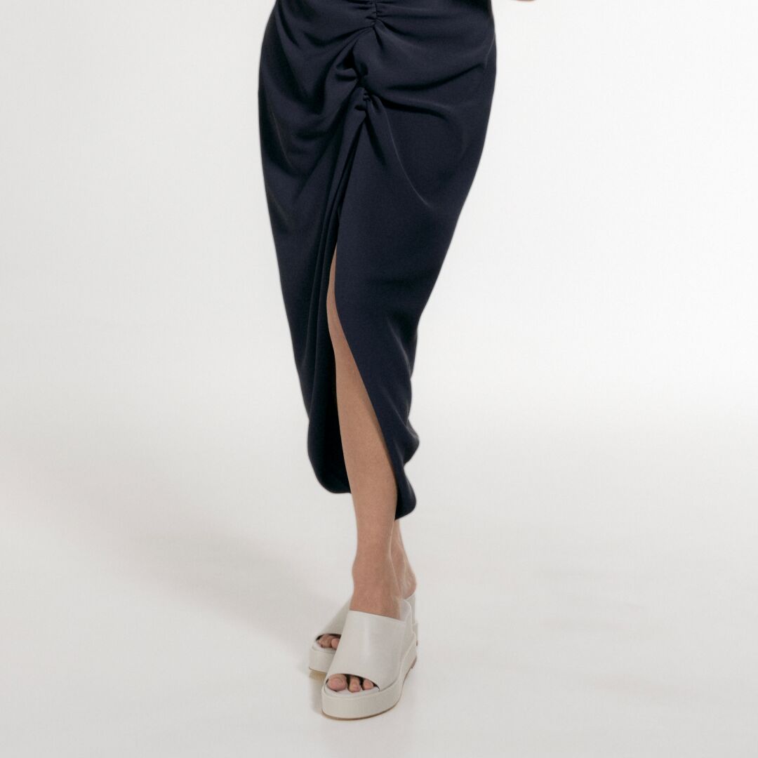 Close-up of a black midi skirt with side slit and white platform sandals on a model.