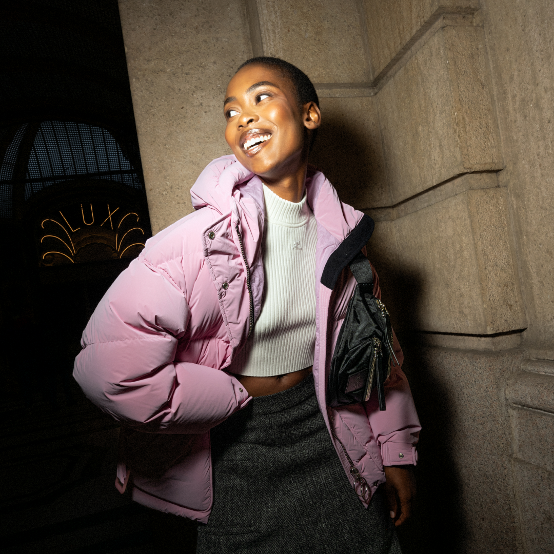 A cheerful model in a pink puffer jacket and stylish accessories, radiating holiday joy in an urban setting.