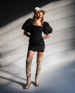 A woman wearing a black dress with puffed sleeves, a hat, and beige thigh-high boots.