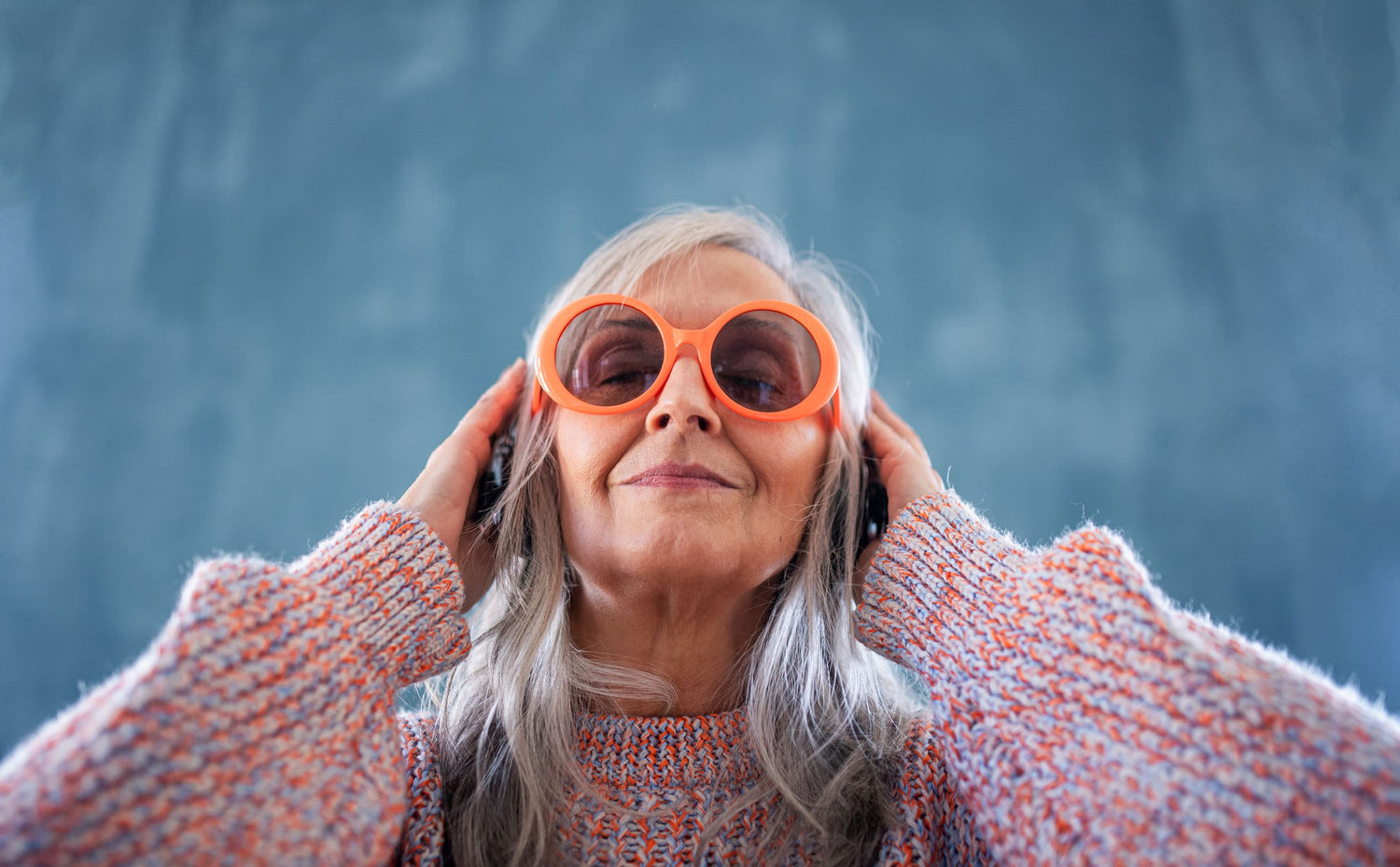 Women's Fall Fashion Over 50, Senior woman with sunglasses standing indoors against dark background, listening to music